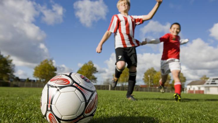 Nahaufnahme eines Fußballs auf einem Rasenfeld, während zwei Kinder im Hintergrund spielen.