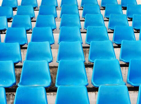Reihe blauer Kunststoffstühle auf einer Tribüne, gleichmäßig angeordnet mit Sicht auf die Sitzflächen.
